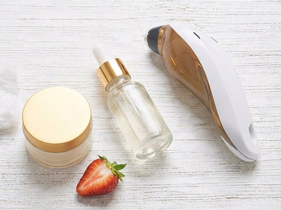 Skincare products, serum bottle, cotton pads, facial device, lime and strawberry on white wood.